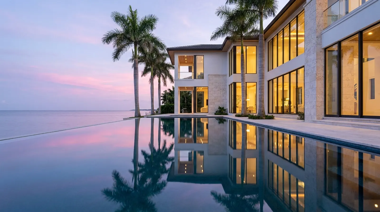 A Gulf-front estate at dusk, every window warmly lit